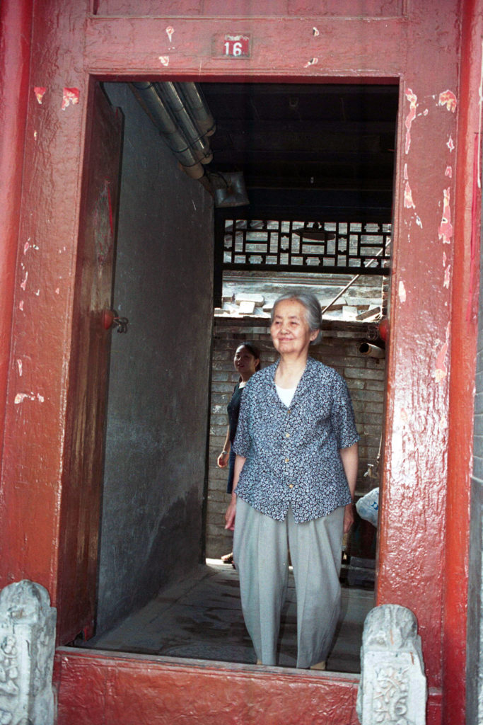 an older Chinese lady standing in the door of her house