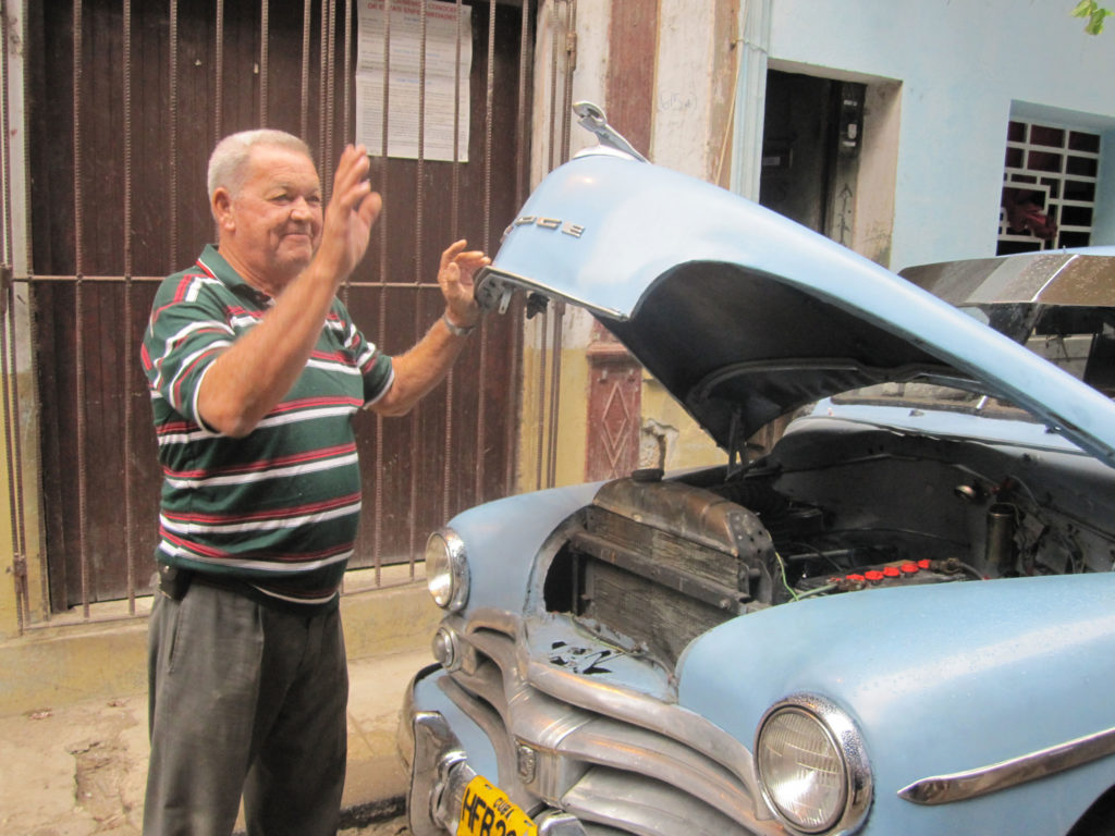 an older man raises the hood on his old car in Havana
