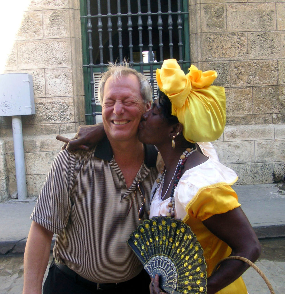 A lady in traditional Cuban dress kisses Chip on the street