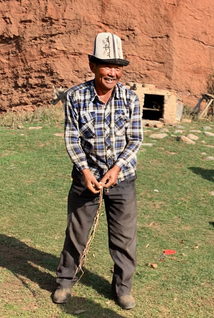 a man in traditional Kyrgyz clothes holding a whip