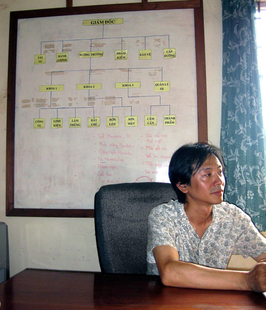 a Chinese man sitting at a desk with a whiteboard behind