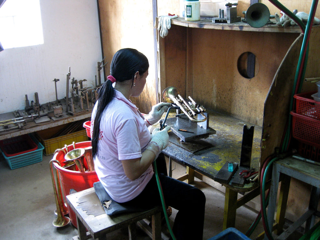 a young lady soldering a trumpet at an old desk