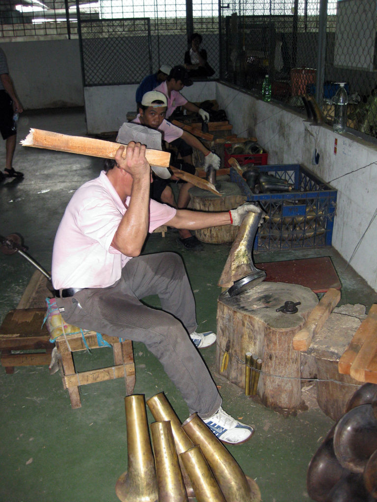 a man with a piece of broken wood beating a brass instrument bell